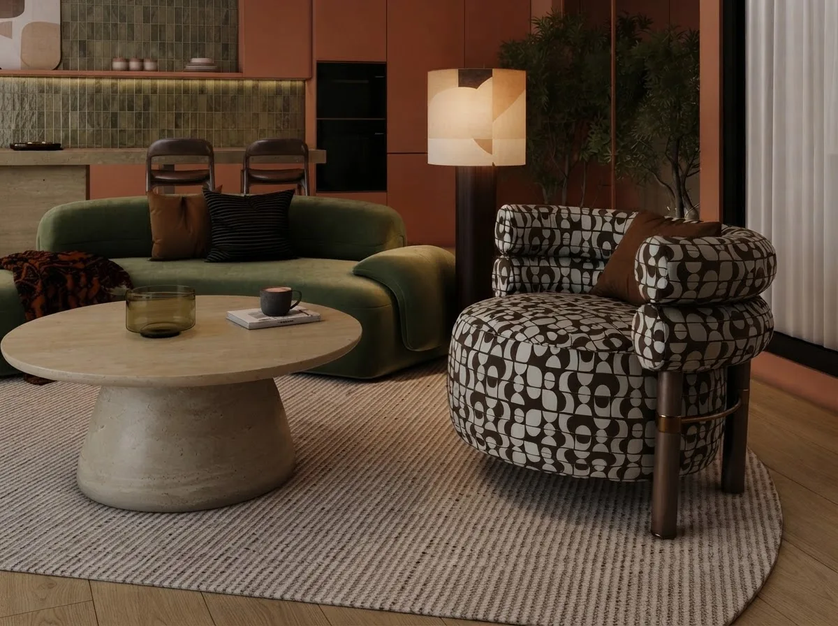 A curved green velvet sofa and a patterned lounge chair grouped around a round stone coffee table on an oval rug, with a floor lamp beside the chair and an open kitchen behind